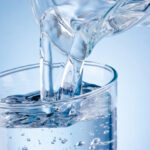 Pouring water from jug into glass on blue background